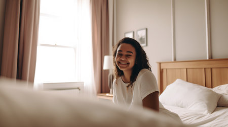 Happy young woman sitting on the bed in her bedroom and smiling.の素材