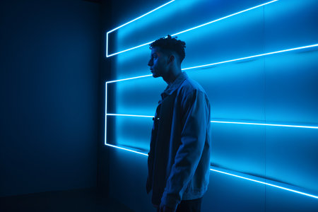 Young man in front of a wall with neon lights. Technology concept.の素材