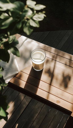 Glass of fresh milk on wooden table with green leaves in garden.の素材
