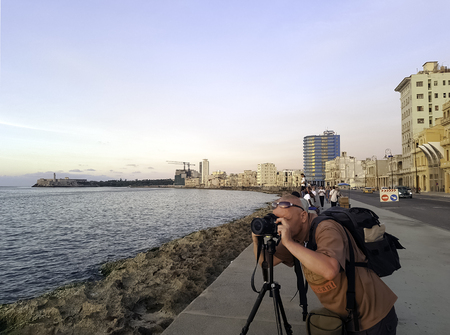 Photographer with camera during sunset with Atlantic Ocean, residential building and Morro Castle in background - Malecon, Havana, Cubaのeditorial素材