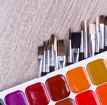 Watercolor paints with set of paint brushes on wooden background