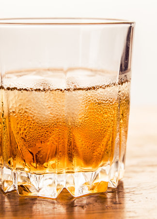 Glass of cold whiskey on wooden surface.