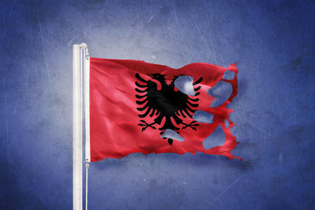 Torn flag of Albania flying against grunge backgroundの写真素材