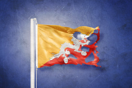 Torn flag of Bhutan flying against grunge backgroundの写真素材