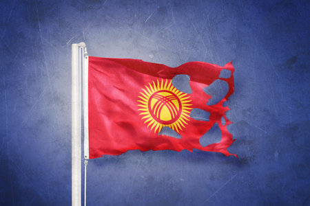 Torn flag of Kyrgyzstan flying against grunge backgroundの写真素材