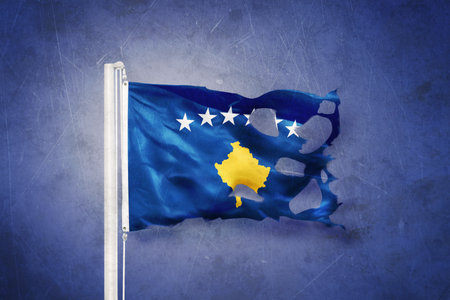 Torn flag of Kosovo flying against grunge backgroundの写真素材