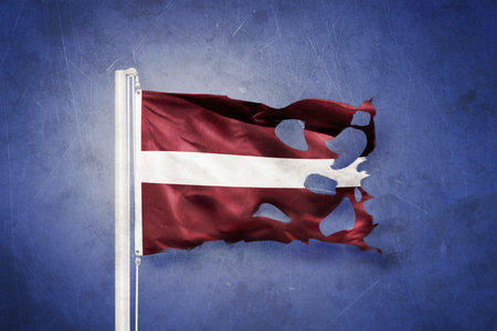 Torn flag of Latvia flying against grunge backgroundの写真素材
