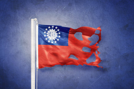 Torn flag of Myanmar flying against grunge backgroundの写真素材