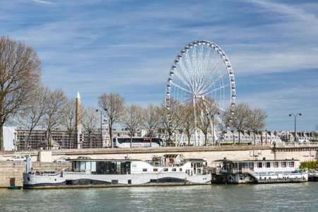 Paris, France, March 30 2017: Riverside in Paris with ferris wheel on Concorde and passenger boat taking tourists on a river cruiseのeditorial素材