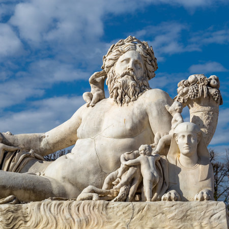 A statue of the Colossus Nile in the Jardin des Tuileries in Paris against a bright blue sky with white cloudsの写真素材