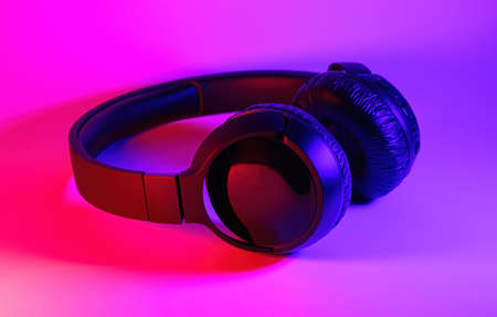 Stylish black wireless headphones lit with colorful neon light on abstract background isolated....