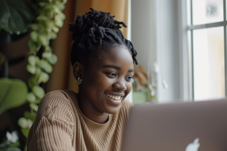 Portrait of smiling biracial female self employed freelancer at work using laptop pc doing research project. Positive motivated young black lady remote student look at camera distracted from learningの素材
