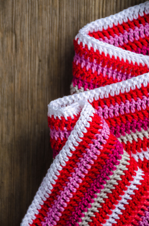 Top view crocheted striped fabric in red colors on the old wood background. Handmade conceptの写真素材
