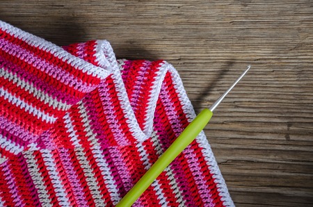 Top view crocheted striped fabric in red colors with crochet hook on the old wood background. Handmade conceptの写真素材