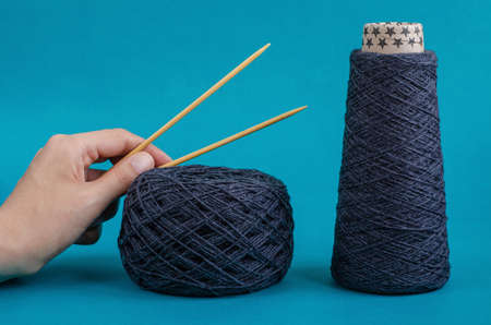 cone of gray wool yarn, yarn ball and female hand with knitting needles on turquoise background....