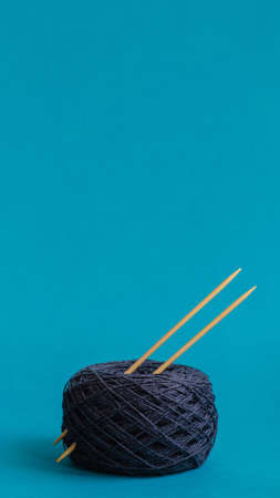 yarn ball of gray wool with knitting needles on turquoise background. copy space