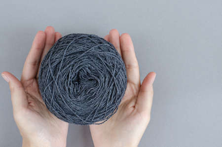 closeup female hands holding ball of gray wool yarn ball on gray background