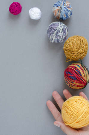 various size and color woollen yarn balls and human hand on gray background. Craft, knitting...