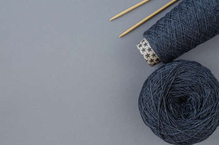 top view cone and ball of gray wool, knitting bamboo needles, notebook and gray pencil on gray...