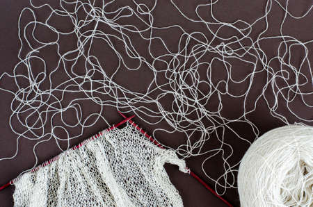 handknitted scarf of lace wool yarn on wood knitting needles and white yarn ball. dark background,...