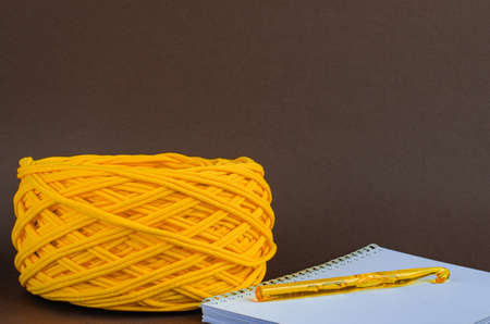 orange t-shirt yarn ball and orange crochet hook on notebook on brown background. Craft, handmade,...