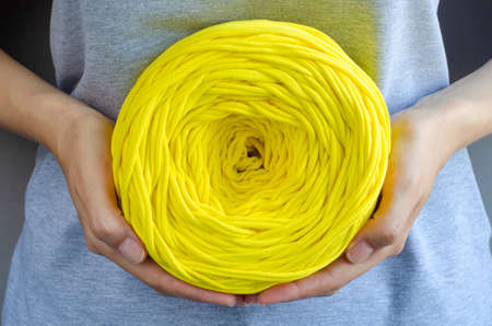female hands holding big yellow t-shirt yarn ball. Handmade, craft, recycle, eco concept