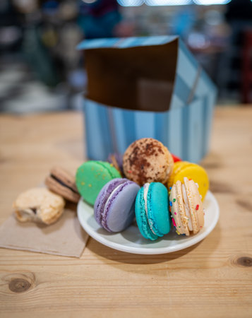 Various flavors of macarons arranged on a plate with a striped takeout box in a cozy cafe.の写真素材