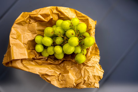 A bunch of green grapes rests on wrinkled brown paper, contrasting with a blue surface.の写真素材