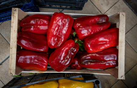 Bright red bell peppers piled in a wooden crate at a market.の写真素材