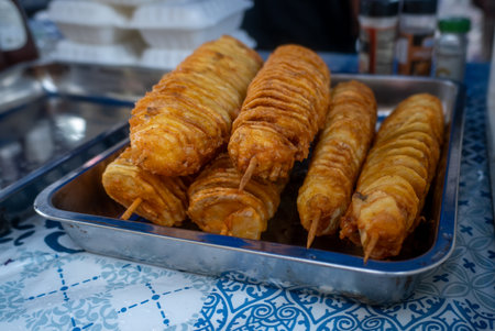 Crispy fried potato skewers arranged on a metal tray at a market.の写真素材