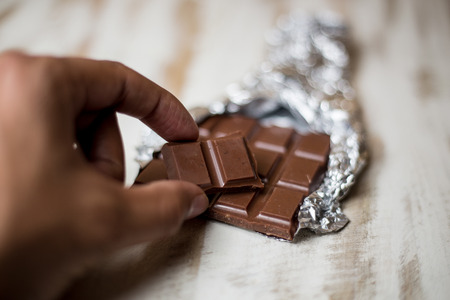 Hand Taking a Piece of Organic Chocolate from a Slab in Foilの写真素材