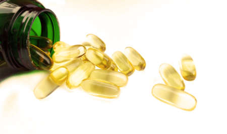 Capsules from fish oil spilling out of pill bottle close-up, on a white backgroundの写真素材