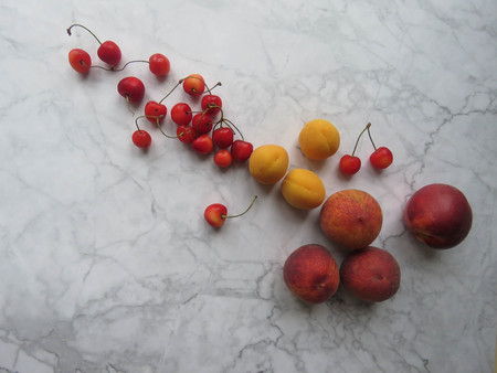 Peaches, apricots and sweet cherries beautifully lie on the tableの写真素材