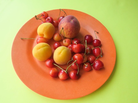 Peaches, apricots and sweet cherries beautifully lie on a plateの写真素材