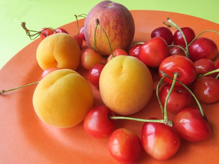 Peaches, apricots and sweet cherries beautifully lie on a plateの写真素材