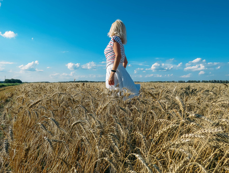 Girl in a bright dress and hat in wheat fieldの写真素材