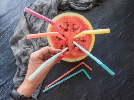 ripe red watermelon with multicolored straws in hand Summer food background healthy eating. eco-friendly products. organic fruits. copyspace. Organic Food. Style Top Viewの写真素材