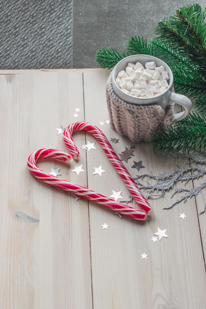 cup in a knitted jacket with two red caramel Christmas candies that lie in the shape of a heart on a white wooden background. Selective focusの写真素材
