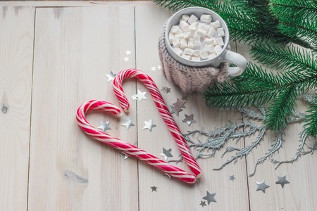 cup in a knitted jacket with two red caramel Christmas candies that lie in the shape of a heart on a white wooden background. Selective focusの写真素材