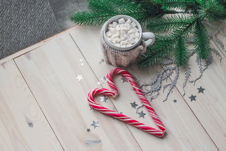 cup in a knitted jacket with two red caramel Christmas candies that lie in the shape of a heart on a white wooden background. Selective focusの写真素材