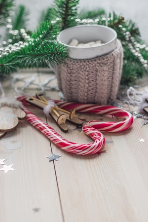 White cup for cocoa in beige knitted clothes. mittens on a white wooden background with christmas tree and red caramel candy space for textの写真素材