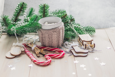 White cup for cocoa in beige knitted clothes. Santa Claus sleigh, mittens, hat, sweater and socks on a white wooden background with christmas tree and red caramel candy space for textの写真素材