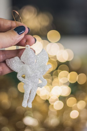 Christmas angel figurine in hand on the background of golden garlands bokeh backgroundの写真素材