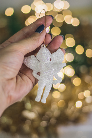 Christmas angel figurine in hand on the background of golden garlands bokeh backgroundの写真素材
