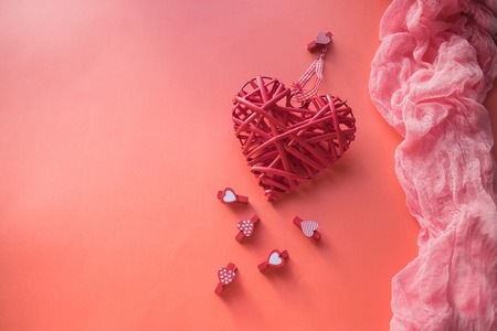 Valentines Day concept. Wicker heart and small clothespins with hearts on a coral background. field for text.