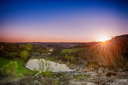 Rural sunset landscape with green hills, lake and sun raysの写真素材