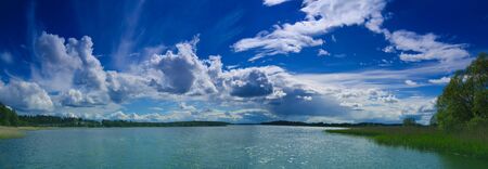 Scandinavian summer lake with deep blue sky and fluffy white clouds, panoramic natural seasonal summer spring backgroundの写真素材