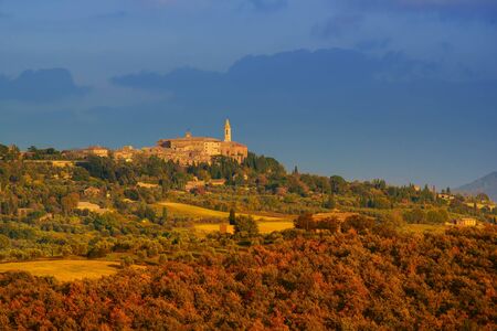 View to the Tuscany medieval city Pienza with colorful trees and fields, at sunsetの写真素材