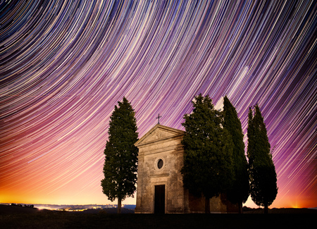 Beautiful Tuscany night landscape with star trails on the sky, cypresses and a chapel. Natural outdoor amazing fantasy background.の写真素材