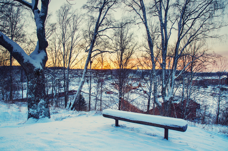 Winter sunset landscape with trees and wooden bench on the hill above city in Sweden, north scandinavian seasonal hipster background.の写真素材